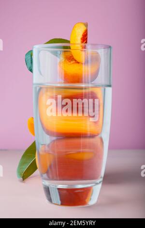 Flying fresh ripe peach in slices, whole fruits with green leaves. Peach fruit levitation on pink color background in frame of water, fruit behind Stock Photo