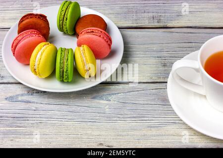 Macarons on a white plate and a cup of tea on a wooden table. French biscuits. Stock Photo