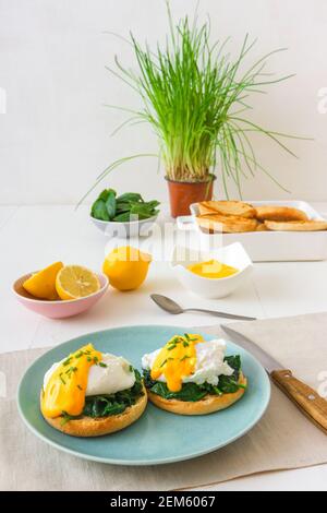 Eggs Florentine, English muffins, spinach, poached eggs, Mornay sauce, chive herbs, lemon, cup of coffee. White wooden table with breakfast. Stock Photo