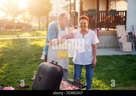 Elderly cheerful couple is standing together and holding each other in front of the vintage grill. Stock Photo