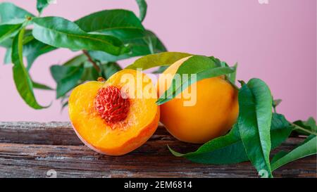 Peaches with leaves on wooden board. Peach in halves with bone