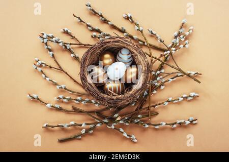 Painted golden and white eggs in the nest with willow twigs on beige background. Easter concept. Top view, flat lay, copy space. Stock Photo