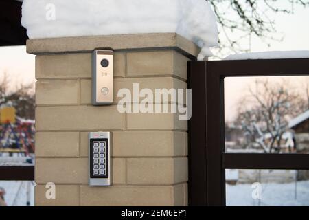 Silver intercom call panel with blue number buttons and a video camera, on a brick beige fence pillar of a private house Stock Photo