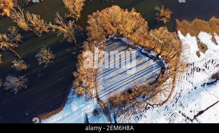 Aerial view from drone of small lake in heart shape with trees next to big lake in winter Stock Photo