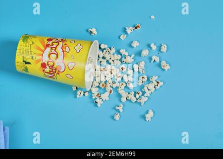 Salty popcorn in paper cup and scattered on blue background Stock Photo