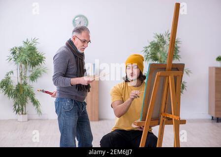 Young man taking lesson from experienced painter Stock Photo
