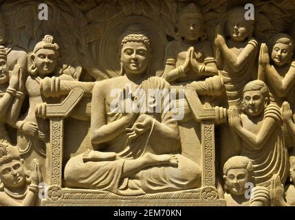 Close-up view of stone carving of Indian god Buddha on throne and being greeted by devotees Stock Photo