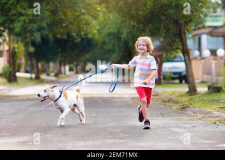 Child walking dog. Kid playing with cute puppy. Little boy running with his pet. Children play in suburban neighborhood street. Animal friends. Friend Stock Photo