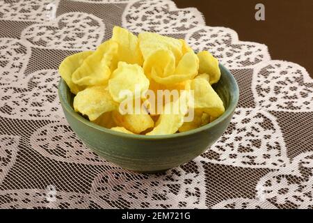 Veal and adjika flavored potato chips in ceramic snack bowl on pink heart table runner on brown tablecloth Stock Photo