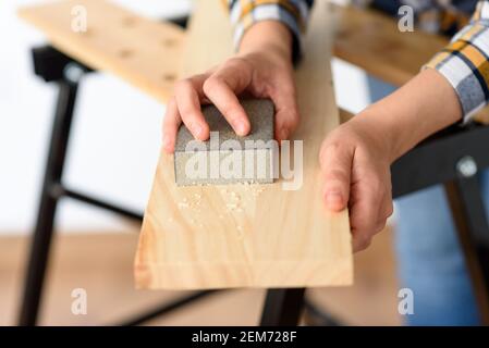 Close-up shot of a woman at home sanding a wood on a workbench. High quality photo. Stock Photo