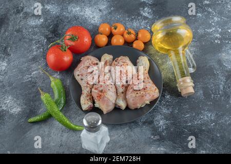 Raw chicken drumstick on black plate with fresh vegetables and spices Stock Photo
