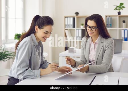 Woman signs a lease or purchase agreement given to her by a bank manager or real estate agent. Stock Photo