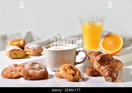 Cup of coffee surrounded by delicious pastries, with an orange juice and half orange at the back on a light background. Traditional breakfast concept. Stock Photo