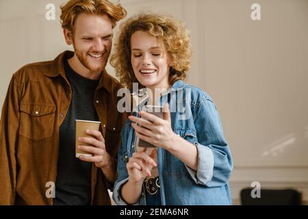 Happy young couple using mobile phones while standing indoors Stock Photo