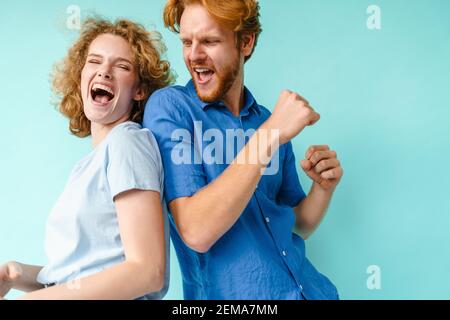 Happy couple of young funny and happy man and woman dancing at studio on blue background Stock Photo