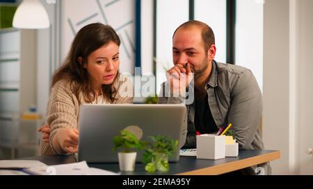 Woman manager pointing on laptop showing new startup idea to coworkers, sitting at desk in modern company office. Diverse colleagues working together for innovative product design in creative studio. Stock Photo