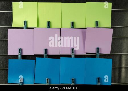 The paper sticky notes hanging from clothespins. Set of multicolored blank square stickers on black background. No people. Stock Photo