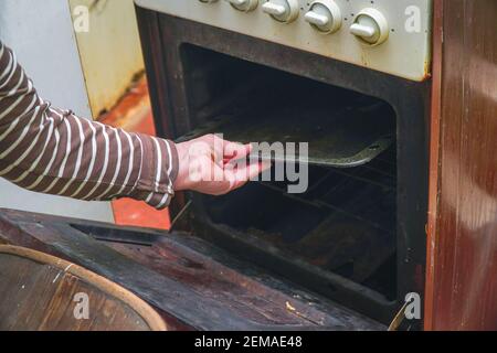 A woman pulls a baking sheet out of the oven of an old gas stove Stock Photo