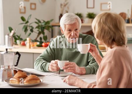 Happy senior couple sitting at the table drinking tea and talking to each other in the kitchen at home Stock Photo