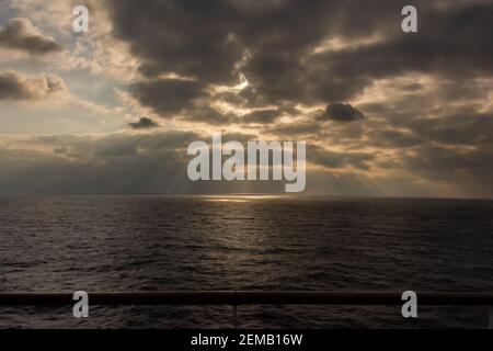 Beautiful scenic views of sun rays bursting through a thick and heavy cloud cover in the middle of the ocean during a cruise. Stock Photo