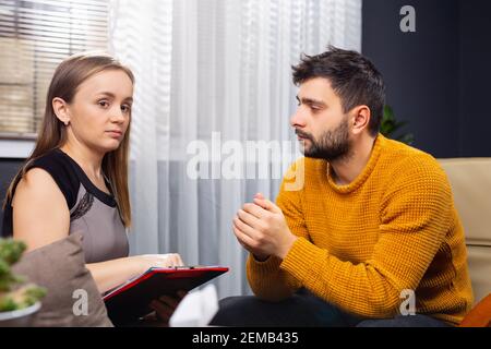 Psychology, mental therapy and middle-age concept - female psychologist with test on clipboard taking notes and listening to businessman patient at Stock Photo