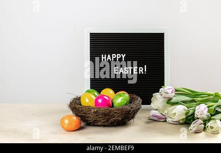 Happy Easter on letter board, painted eggs, and tulips. Holiday concept Stock Photo