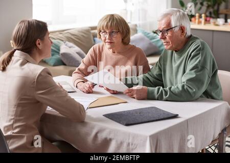 Senior couple sitting at the table with financial advisor reading documents and consulting in the room Stock Photo