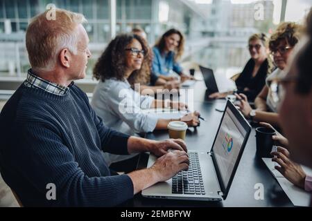 Senior businessman using laptop and discussing new project with team. business people sitting around table in boardroom and having a meeting. Stock Photo