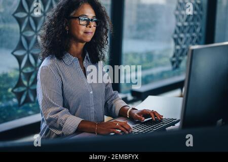 Woman sitting at her desk in office and working on computer. Mature businesswoman working at her office desk. Stock Photo