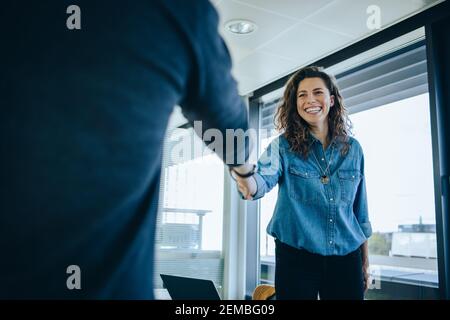 Businesswoman shaking hands with a job applicant in meeting room. Smiling female entrepreneur shaking hands with a male candidate for job interview. Stock Photo