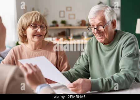Happy senior couple signing a contract and talking to consultant during meeting at home Stock Photo