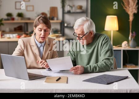 Young businesswoman consulting senior man about financial documents using laptop while they sitting at the table at home Stock Photo