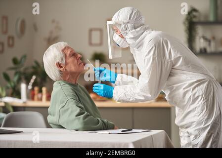 Senior man passing coronavirus test with doctor in protective suit taking an analysis at home Stock Photo