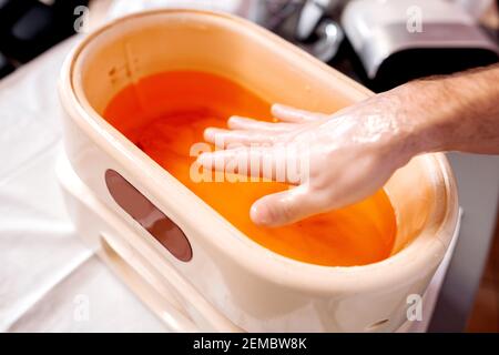 Close up of a male hand taken out from a paraffin bath during manicure treatment, pretty hands Stock Photo