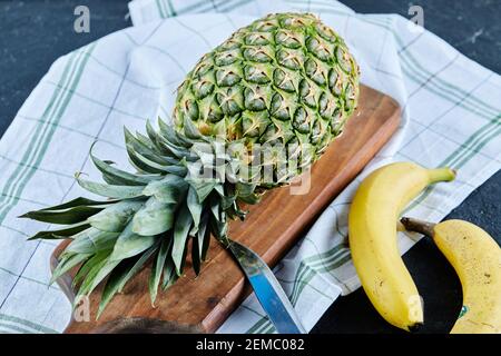 Ripe pineapple with bananas on wooden board with white tablecloth Stock Photo