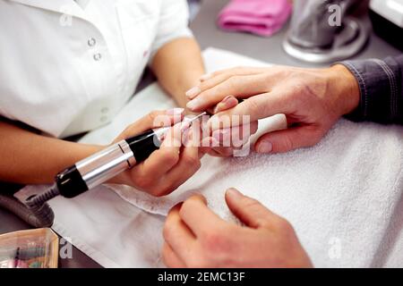 Manicurist using electric nail file on the nails of her customer, neat nails Stock Photo