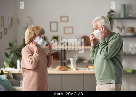 Senior couple standing opposite each other and wearing protective masks while standing in the room Stock Photo