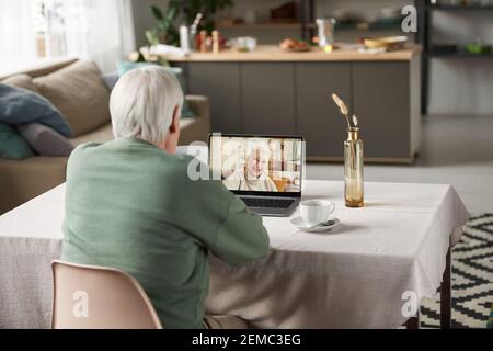 Rear view of senior man using laptop for online communication with woman while sitting at the table in the room Stock Photo