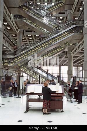 Archive 1996 historical inside view of the ground floor of the insurance and reinsurance market Underwriting Room at the Lloyds of London business building with woman standing looking at the famous loss book in modern interior structure and escalator system beyond in City of London England UK a 1990s archival image Stock Photo