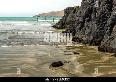 Seawater gently beating against the rocky coastline at Okains Bay, Banks Peninsula, South Island, New Zealand. Stock Photo