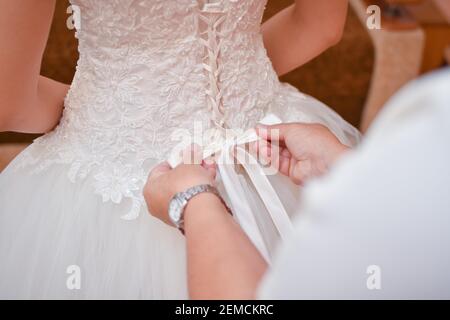 Wedding dress, corset. Mom ties a bow on the bride's dress. Rear view. Stock Photo