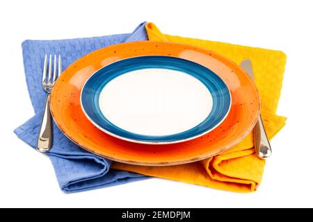Two colorful empty plates with knife and fork on blue and yellow cotton towels isolated on white background. Stock Photo
