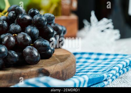 A cluster of black grapes on wooden plate with blue tablecloth Stock Photo