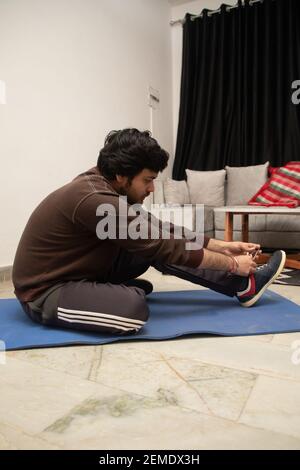 Asian Indian man gaming, streaming and watching TV alone in living room on a grey sofa and white table. Stock Photo