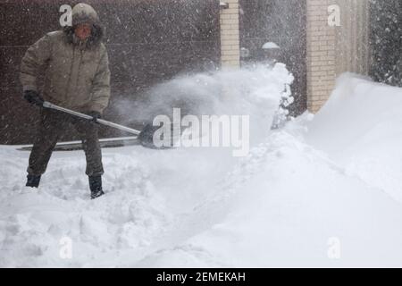 man throws snow from the front yard of his own house with a plastic shovel during a heavy snowfall. Stock Photo