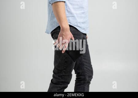 Stylish handmade black leather wallet in a mens hand in blue shirt and black jeans on white background. Stock Photo