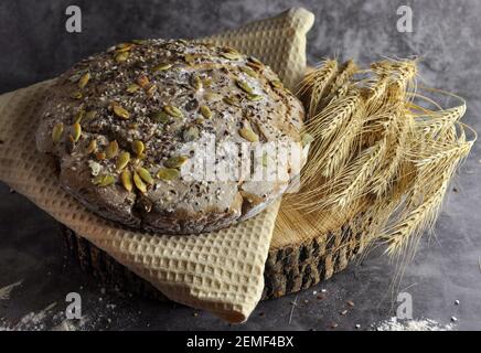 Bread with seeds. A loaf of bread, covered with white flour, on a wooden board. Dark background. Close up view. Stock Photo