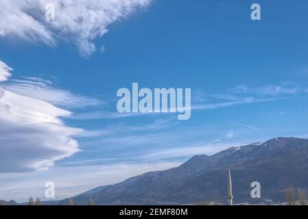 Magnificent mountain (uludag) view from city center together with minaret of mosque and dried trees. Huge clouds and snow remains on top of mountain. Stock Photo