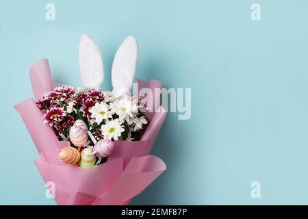 Happy Easter - flowers and colourful eggs with white bunny ears on blue background, copy space Stock Photo