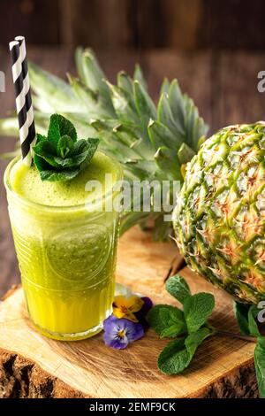 Green smoothie with pineapple in background placed on the wooden stump Stock Photo
